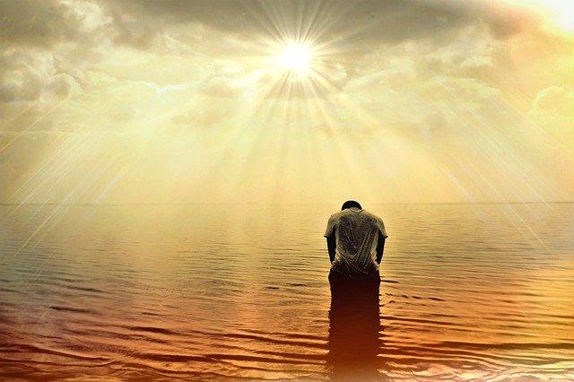 Standing in water with head bowed in prayer under sun beams